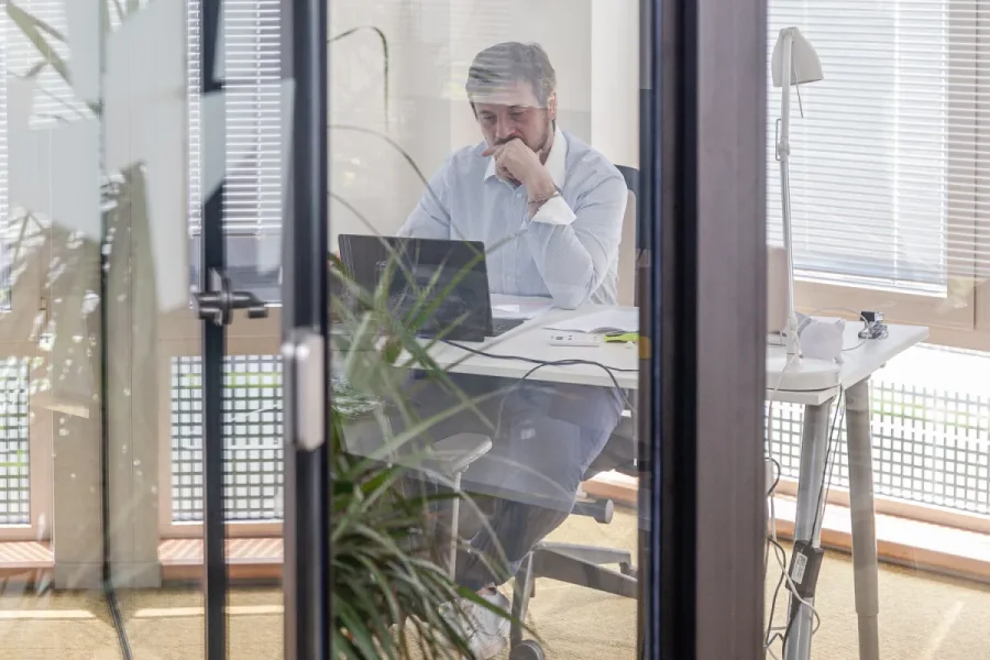 Consultant working at a laptop behind a glass office partition